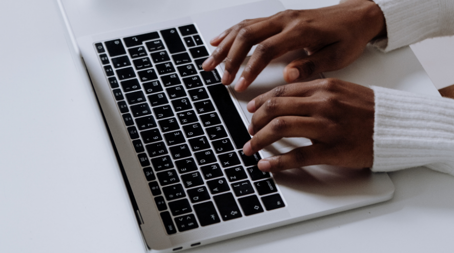 Black woman's hands typing on a silver laptop with black keys