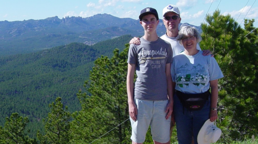 Family photo of David, Bruce and Liz standing in front of trees and a mountains.