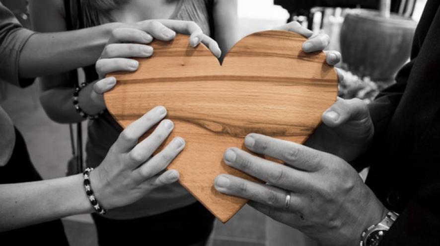 Black and white photo of people holding a wooden heart, which is in colour