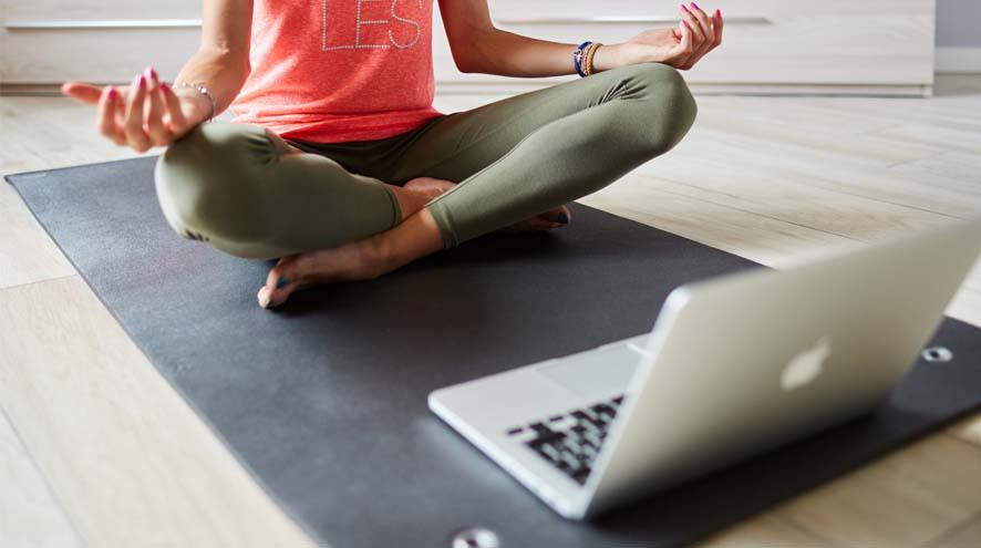 Girl seated practicing yoga in front of a laptop 