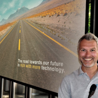 Image of Chris Bint, CEO and chief learning officer for Tech coaches, in front of a sign of the open road.
