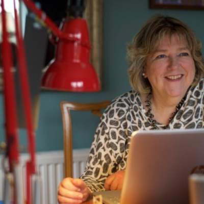 Prof. June Andrews sitting at her desk with a red reading lamp, a gold mirror and a laptop