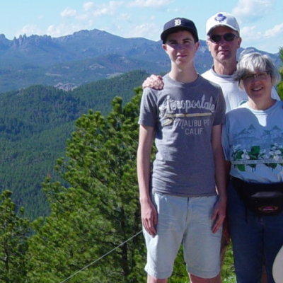 Family photo of David, Bruce and Liz standing in front of trees and a mountains.