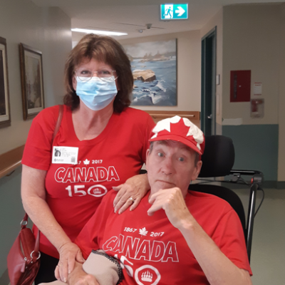 Woman with dark shoulder-length hair wearing a Canada 150 shirt resting on a man in a wheelchair wearing the same shirt